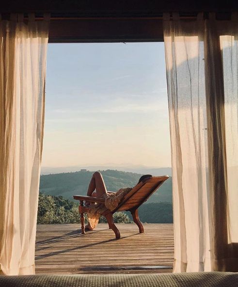 Guest reclining on a wooden lounger gazing at misty hills through sheer curtains